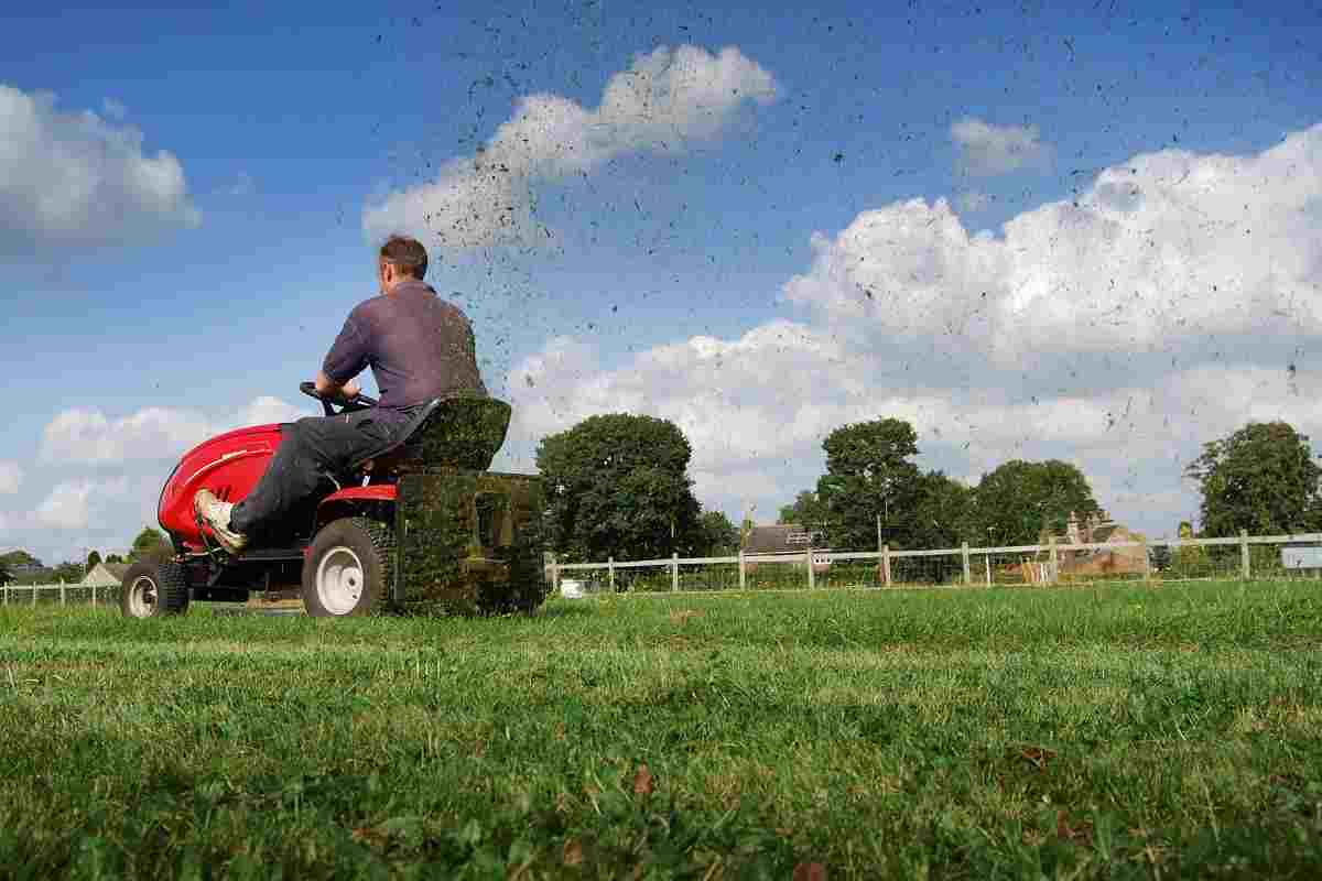 Man cutting the lawn with grass cuttings spraying from the back of the mower.